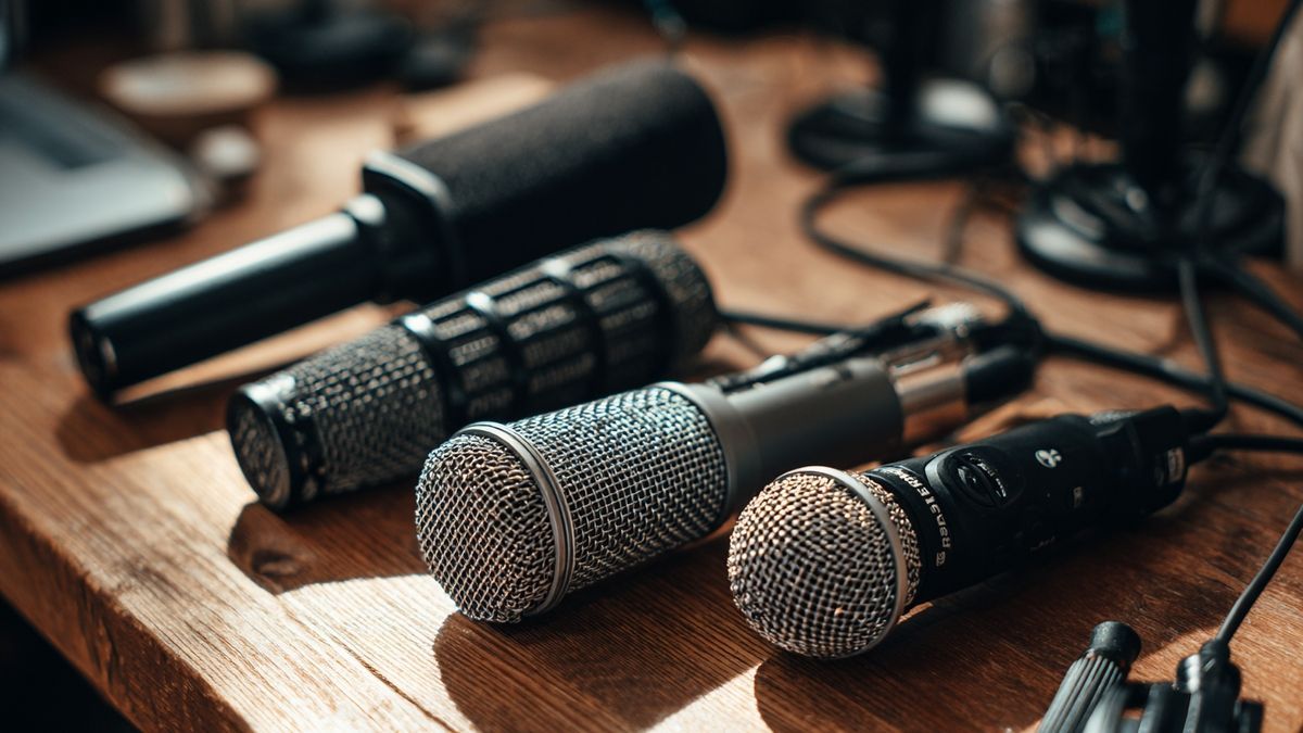 Artistic display of diverse microphones and recording equipment on a wooden desk within a home studio.
