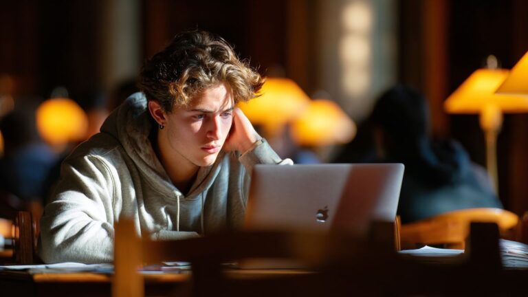 A student immersed in studying with their laptop featuring an AI chatbot in the renowned Harvard library.