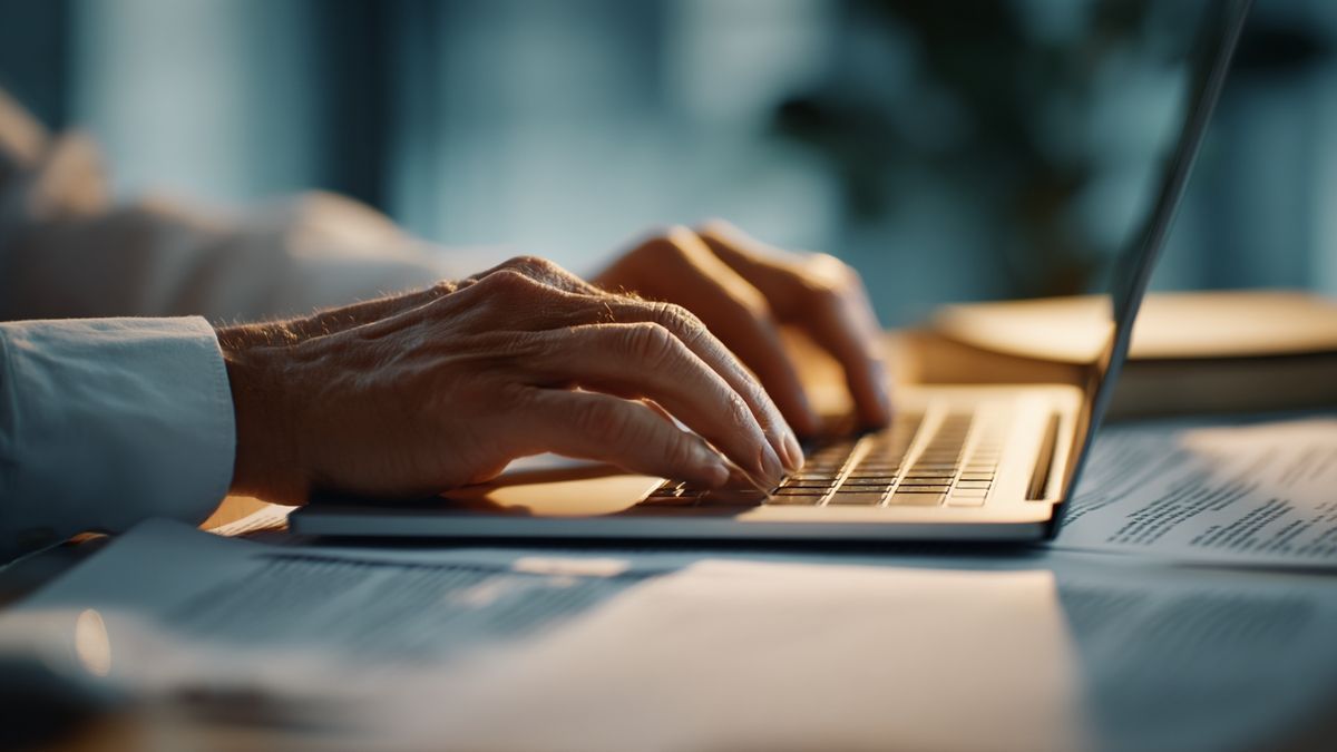 Individual typing on a laptop surrounded by papers on hybrid AI and reasoning techniques